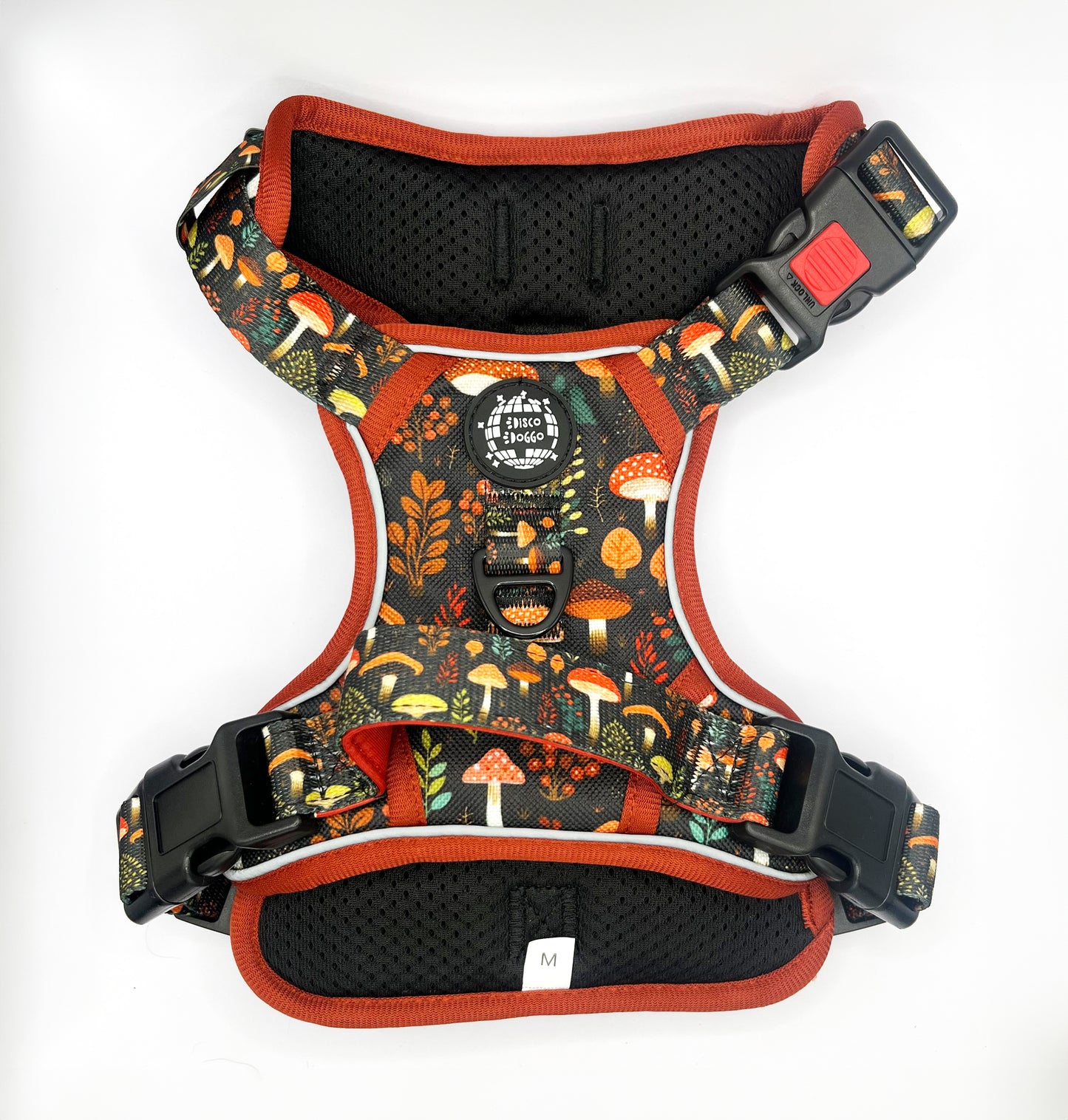 Adjustable technical dog harness featuring an intricate mushroom pattern over a durable fabric. The harness is equipped with heavy-duty buckles for secure fastening, reflective strips for nighttime visibility, and a reinforced handle on the back for better control. The design is complemented with breathable mesh lining for comfort, and multiple attachment points for leashes. The colorful mushroom illustrations add a playful touch to the practical design, suitable for outdoor activities and training sessions