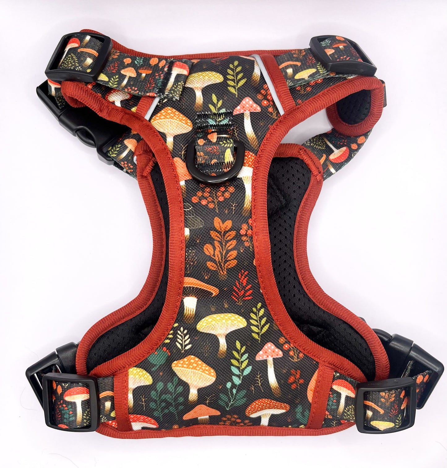 Adjustable technical dog harness featuring an intricate mushroom pattern over a durable fabric. The harness is equipped with heavy-duty buckles for secure fastening, reflective strips for nighttime visibility, and a reinforced handle on the back for better control. The design is complemented with breathable mesh lining for comfort, and multiple attachment points for leashes. The colorful mushroom illustrations add a playful touch to the practical design, suitable for outdoor activities and training sessions